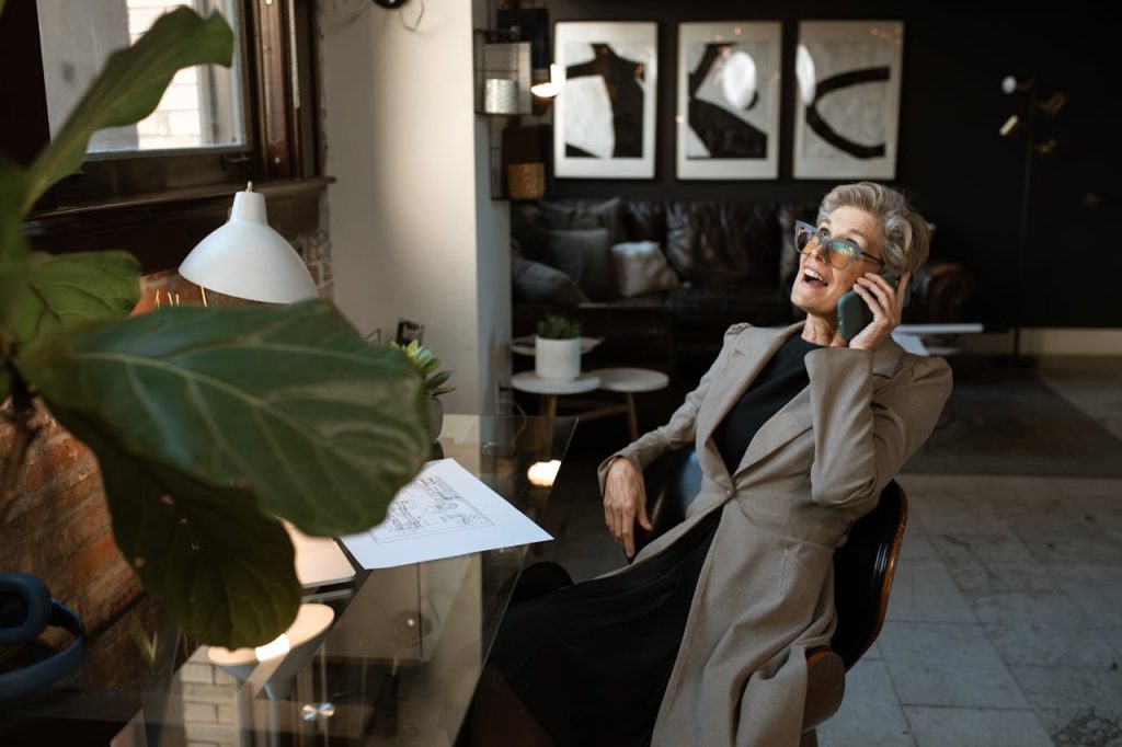 Senior woman in a modern office setting, smiling while on a phone call. Stylish and professional workspace.